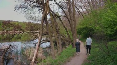 Huzurlu bir bahar gününde yaşlı bir kadın ve torunu göl kenarındaki orman yolunda yürüyorlar. Yüksek kalite 4k görüntü