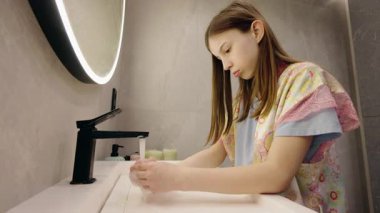Genç kız, modern bir banyoda ellerini su ve sabunla yıkıyor ve hijyene odaklanıyor. Yüksek kalite 4k görüntü