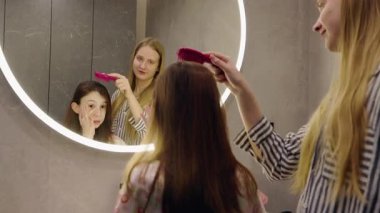 Genç bir kız aynanın karşısına geçip yüz kremi sürerken ablası da arkasında durup gülümseyerek kendine bakmanın keyfini çıkarıyor. Yüksek kalite 4k görüntü