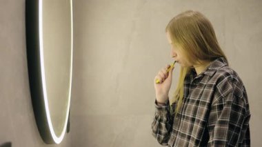 Genç bir kız, parlak, modern bir banyoda dişlerini fırçalıyor. Güne basit bir sabah bakımıyla başlıyor. Yüksek kalite 4k görüntü