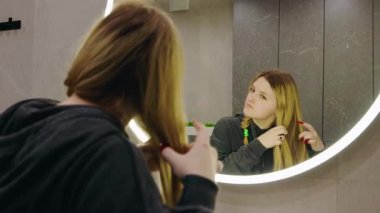 Modern banyoda, yuvarlak aynanın önünde saçını ören sarışın bir genç kız. Yüksek kalite 4k görüntü