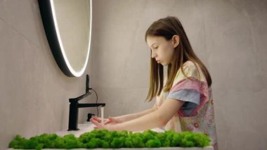 Genç kız modern bir banyoda yuvarlak bir aynayla ellerini akarsu altında dikkatlice yıkıyor. Yüksek kalite 4k görüntü