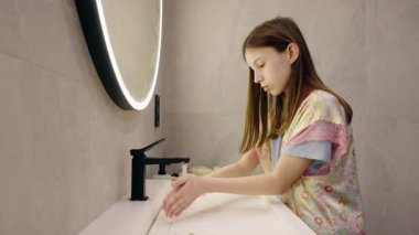 Genç kız, modern, parlak bir banyoda, parlak bir aynayla akan suyun altında ellerini iyice yıkıyor. Yüksek kalite 4k görüntü