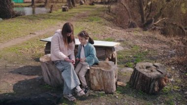 İki kız kardeş kırsal kesimde tahta kütüklerde oturuyor güneşli bir bahar gününde yaşlı kızların ellerinde bir şeye bakıyorlar..