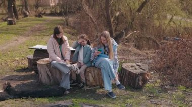 Farklı yaşlarda üç kız kırsal kesimde ağaç kütüklerinde dinlenirken, biri telefon kullanırken diğerleri yakınlarda oturup anın tadını çıkarıyor. Yüksek kalite 4k görüntü
