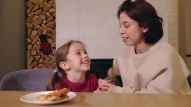Anne ve kızı yemek masasında birlikte neşeyle gülüyor, el ele tutuşuyor ve sıcak, mutlu bir aile anını paylaşıyorlar. Yüksek kalite 4k görüntü