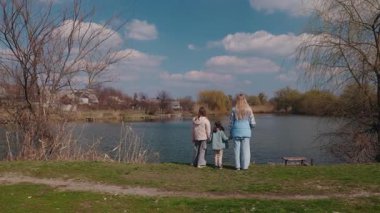 Farklı yaşlarda üç kız, bir köyün gölü kenarında el ele durur ve huzur dolu bahar manzarasına hayran kalırlar. Yüksek kalite 4k görüntü