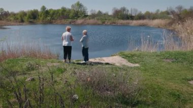 Güneşli bir bahar gününde sakin bir gölün kenarında duran iki yaşlı kadın birlikte doğanın tadını çıkarıyorlar. Yüksek kalite 4k görüntü