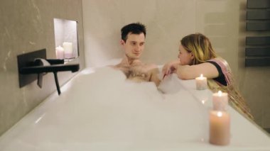 Sıcak banyo zamanında köpük ve mum ışığında dinlenen romantik genç çift. Yüksek kalite 4k görüntü