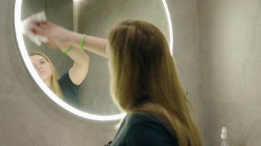 Genç sarışın kadın fayanslı bir banyoda aynadan çıkan mermiyi dikkatlice temizliyor. Yüksek kalite 4k görüntü