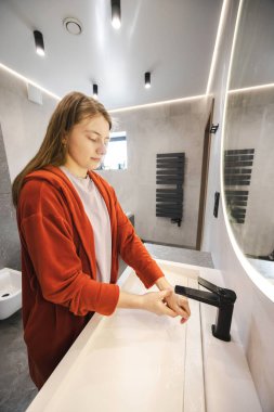 Kırmızı bornozlu genç bir kadın modern bir lavaboda, parlak bir banyoda ellerini dikkatlice yıkıyor. Yüksek kalite fotoğraf