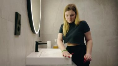 Genç sarışın bir kadın siyah bir musluğun yanında beyaz bir banyo lavabosunu siliyor ve temizlik malzemelerini temizliyor. Yüksek kalite 4k görüntü