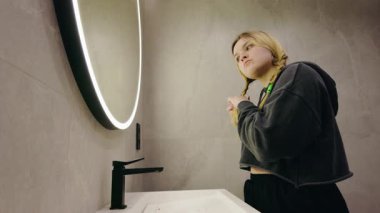 Genç kız modern banyoda parlak aynanın yanında dikilirken örgü örüyor. Yüksek kalite 4k görüntü