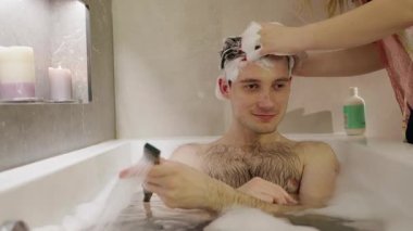 Genç bir adam, kız arkadaşı saçlarını şampuanla yıkarken ve nazikçe kafa derisine masaj yaparken banyo yapmaktan zevk alır. Yüksek kalite 4k görüntü