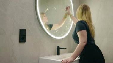 Modern mermiyi temizleyen genç bir kadın şık bir banyoda aynayı aydınlatıyor. Yüksek kalite 4k görüntü