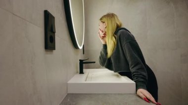 Sarışın genç kız şık banyoda parlak aynanın önünde saçını düzeltiyor. Yüksek kalite 4k görüntü