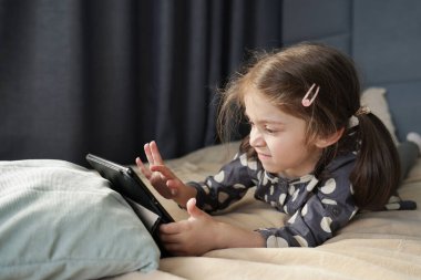Küçük kız, yatakta tablet ekranı tıkırdatırken hayal kırıklığına uğruyor. Yüksek kalite fotoğraf