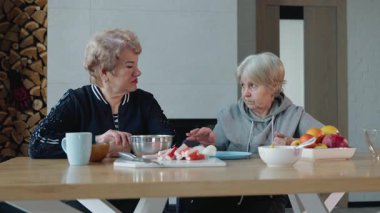 İki yaşlı kadın sıcak bir mutfakta ev yapımı yemek hazırlıyor, ahşap bir masada malzemeleri kesiyorlar. Yüksek kalite 4k görüntü