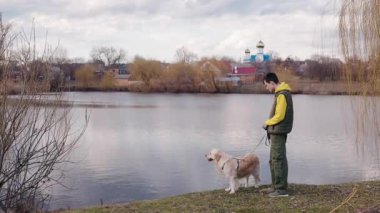 İnsanlar ve Golden Retriever nehir kıyısında huzurlu bir anın tadını çıkarıyorlar. Manzaralı köy evleri ve su üzerinde görülebilen bir kilise var. Yüksek kalite 4k görüntü