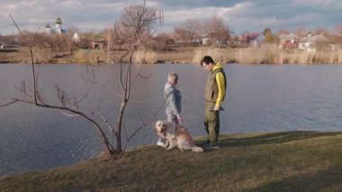 Genç bir adam ve yaşlı bir kadın kırsal bir köyde huzurlu bir göl kenarında Golden Retriever 'da yürüyor. Yüksek kalite 4k görüntü