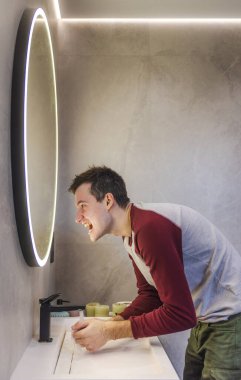Genç adam ellerini yıkarken aynaya doğru bağırıyor, yoğun duygularını ifade ediyor ya da modern bir banyo ortamında kendini havaya sokuyor. Yüksek kalite fotoğraf