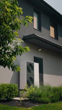 Çevresi yeşilliklerle çevrili ve peyzaj bahçesindeki ağaç dalları tarafından gölgelenmiş bir ev duvarındaki enerji tasarruflu bir ısı pompasının dikey görüntüsü. Yüksek kalite 4k görüntü