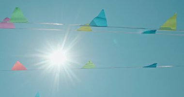 Pastel renkli üçgen bayraklar bulutsuz mavi bir gökyüzünün altında dalgalanıyor. Güneş arkadan ışıldıyor, ılık ve tasasız yaz günlerini anımsatıyor. Yüksek kalite 4k görüntü
