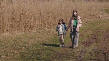 İki kız kardeş, el ele tutuşarak ve bahar kırsalında birlikte sakin bir anın tadını çıkararak çimenli kırsal bir yolda yavaşça yürürler. Yüksek kalite 4k görüntü
