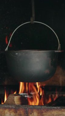 Black cast iron pot hanging over an open fire in a rustic fireplace for traditional cooking. High quality 4k footage
