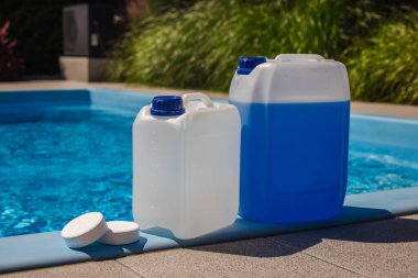 Temiz bir yüzme havuzunun kenarına klor tabletleri yerleştirilmiş beyaz ve mavi kimyasal kaplar, su dezenfeksiyonu ve düzenli havuz bakımı için kullanılır. Yüksek kalite fotoğraf