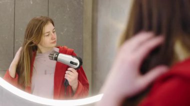 Genç bir kız aynanın önünde saç kurutma makinesiyle saçını şekillendiriyor. Yüksek kalite 4k görüntü