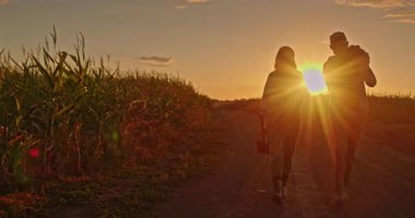 Gün batımında birlikte yürüyen çiftçi çift, bir kürek taşıyan kadın ve omzunda altın ışığa karşı silueti olan patates çuvalı tutan bir adam. Yüksek kalite 4k görüntü