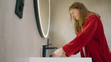 Kırmızı bornozlu genç kız, günlük hijyen rutininin bir parçası olarak evde yüzünü yıkıyor. Yüksek kalite 4k görüntü