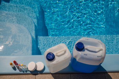 Havuz bakımı malzemeleri, klor tabletleri, test seti şişeleri ve temiz mavi havuzun kenarına yerleştirilmiş büyük kimyasal kaplar dahil. Yüksek kalite fotoğraf