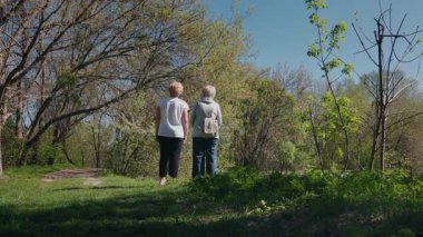 İki yaşlı kadın yemyeşil bir bahar ormanında dikiliyorlar. Bir tanesi ağaçlardaki bir şeyi işaret ediyor ve çevrelerindeki doğanın tadını çıkarıyor. Yüksek kalite 4k görüntü