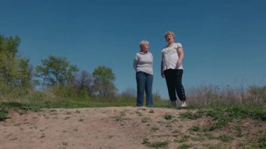 İki yaşlı kadın kumlu bir yamacın tepesinde durmuş, açık mavi bir gökyüzünün altında bahar yürüyüşleri sırasında duraksıyorlar. Yüksek kalite 4k görüntü