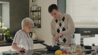 Yaşlı bir kadın, yetişkin torun mutfakta gözlemlerken ve yardım ederken bir tavada şerbet çeviriyor. Yüksek kalite 4k görüntü