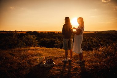 Anne huzurlu bir kırsal alanda altın bir günbatımında genç kızlarının saçlarını nazikçe tarar. Yüksek kalite fotoğraf