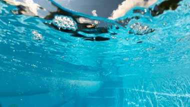 Su altında yüzey gerilimini ve suyun altından gökyüzü bulutlarını gösteren basamakları, kabarcıkları ve parıldayan yansımaları olan bir su altı havuzu. 