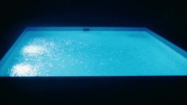 Şiddetli yağmurun altında, su yüzeyine damlayan gözle görülür yağmur damlaları eşliğinde geceleri parlayan aydınlık yüzme havuzu. Yüksek kalite 4k görüntü