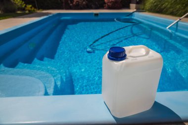 Havuzun kenarına mavi kapaklı, parlak temiz yüzme havuzu ve arka planda görünen vakum hortumu olan beyaz plastik plastik bir kimyasal kap. Yüksek kalite fotoğraf
