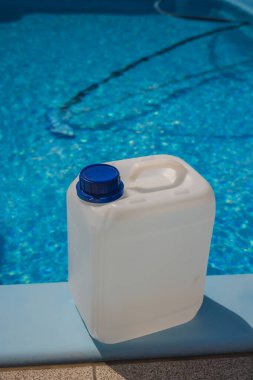 Parlak mavi bir yüzme havuzunun kenarına yerleştirilmiş, havuz suyu arıtma ve bakımında kullanılan beyaz plastik bir kimyasal kap. Yüksek kalite fotoğraf