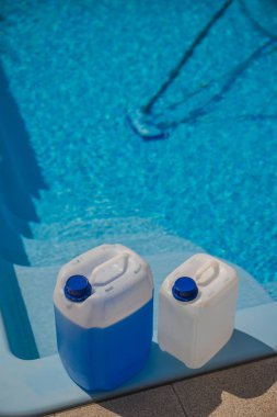 Rutin bakım sırasında temiz mavi bir havuzun yanında duran mavi yüzme havuzu kimyasal deposu için kullanılan büyük plastik sürahiler. Yüksek kalite fotoğraf