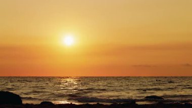 Sakin denizin üzerinde altın bir gün doğumu, yumuşak dalgalar ve berrak bir ufukla. Yüksek kalite 4k görüntü