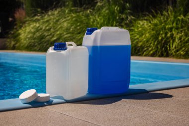Güneşli bir günde, havuz kenarında mavi ve beyaz kimyasal kaplar ve etrafa saçılmış klor tabletleriyle temiz bir yüzme havuzu. Yüksek kalite fotoğraf