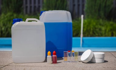 Havuz bakımı malzemeleri, kimyasal kutular, klor tabletleri, damlatıcı şişeler ve güneş ışığında bir yüzme havuzunun yanına yerleştirilmiş su test seti. Yüksek kalite fotoğraf