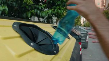 Genç adam Roma 'da bir sokakta sarı bir konteynırda boş plastik şişeleri geri dönüştürüyor. Yüksek kalite 4k görüntü