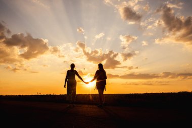 Gün batımında, güneş ışınlarıyla dramatik bulutların arasından el ele tutuşan iki siluet içinde kadın. Yüksek kalite fotoğraf