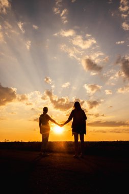 Gün batımında el ele tutuşan iki kadın dramatik güneş ışınları bulutları delip geçiyor. Yüksek kalite fotoğraf