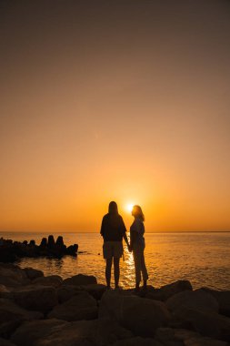 Gün doğumunda el ele tutuşan iki kadın deniz ufkuna bakıp aile bağlarını, duygusal sağlığı, aşkı ve doğayla barışçıl bağları sembolize ediyor. Yüksek kalite fotoğraf